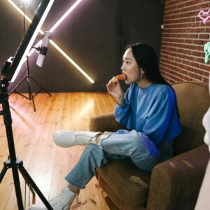 A young woman eats pizza while streaming in a stylish indoor setup with neon lights.