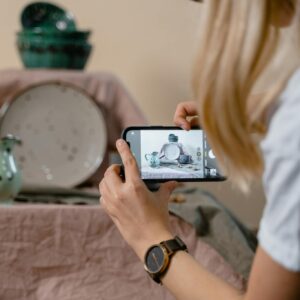 Person photographing elegant ceramic crockery setup with mobile phone for online selling.