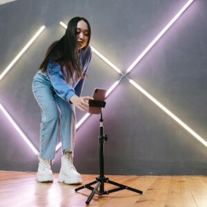 Young Asian woman setting up smartphone for streaming indoors with neon lights.